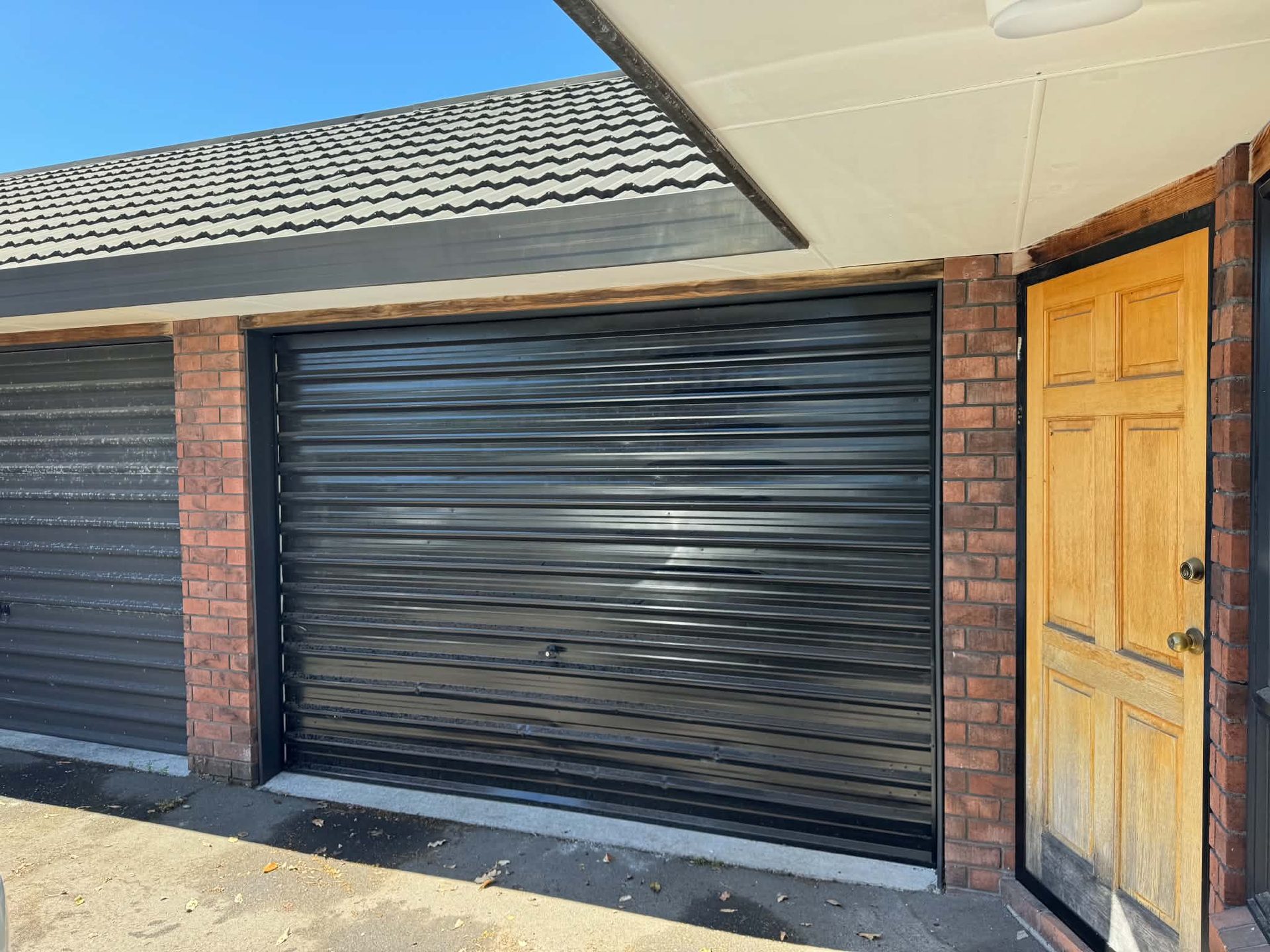 Dark roller garage door with coated tile roof above